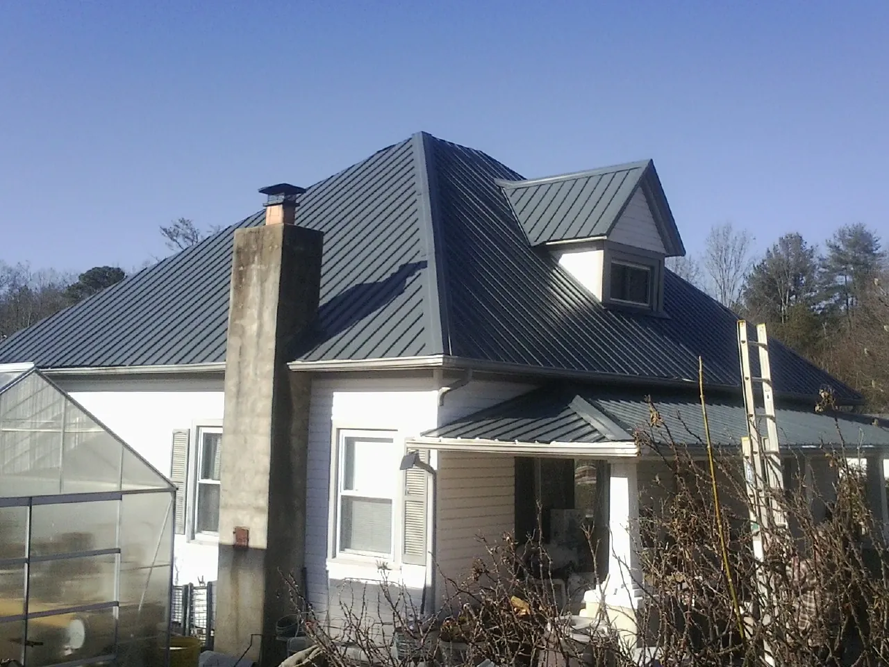 Dark blue standing seam metal roof on a white farmhouse with dormer — Slate & Tile Roof Repair by Roofing Brothers in Foxburg