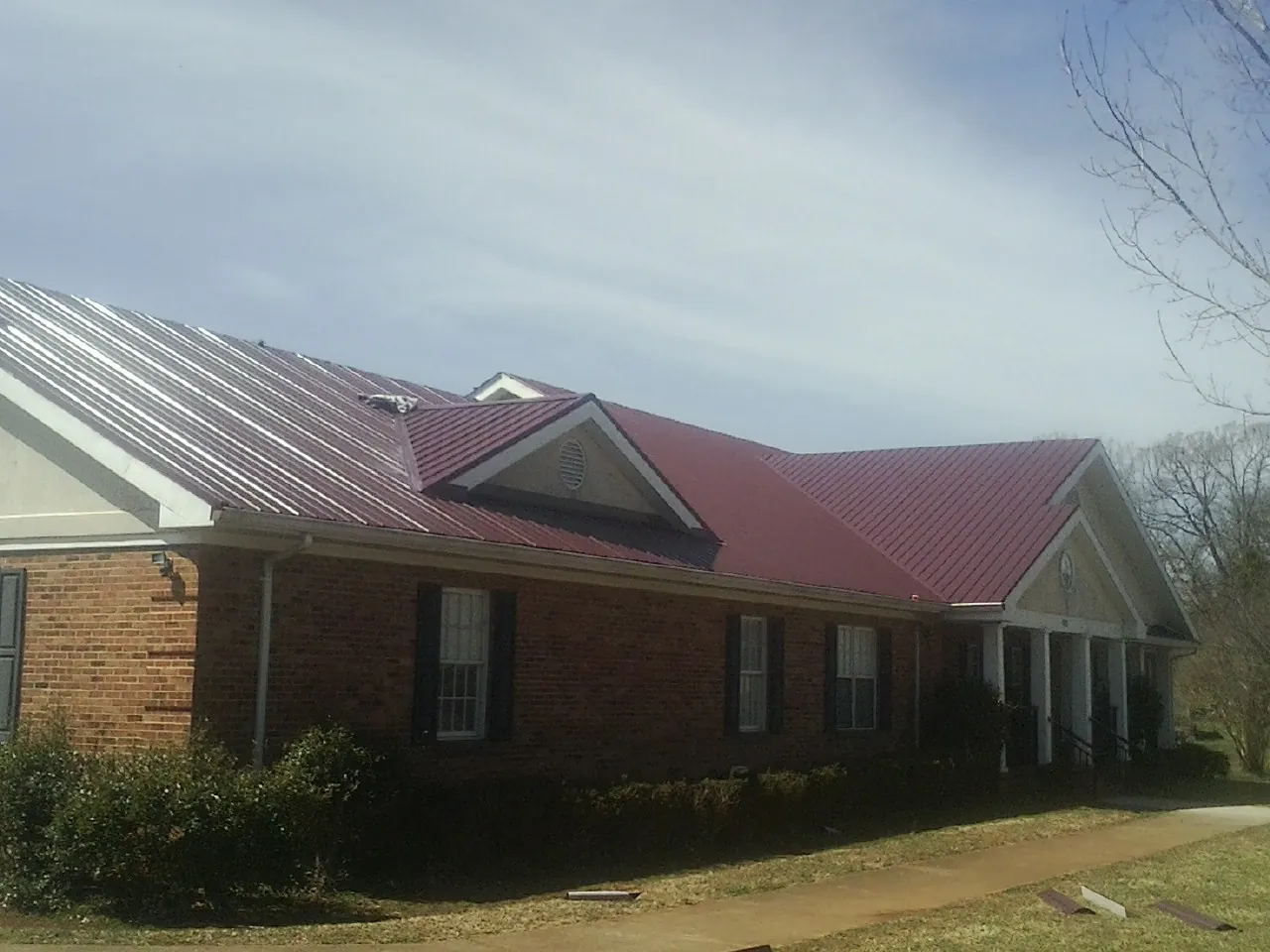 Red metal roof with gabled entries on a long brick building, from a Hail Damage Roof Repair job in Foxburg