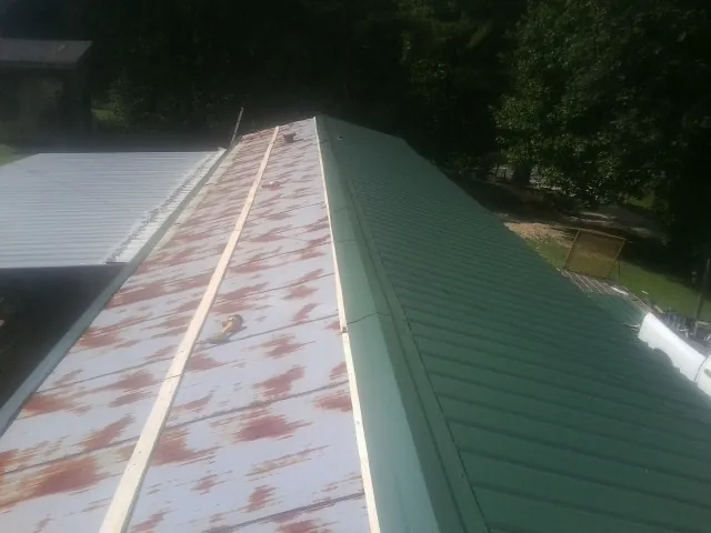 Old rusted panels beside newly installed green metal roofing — Wind Damage Roof Repair by Roofing Brothers in Foxburg