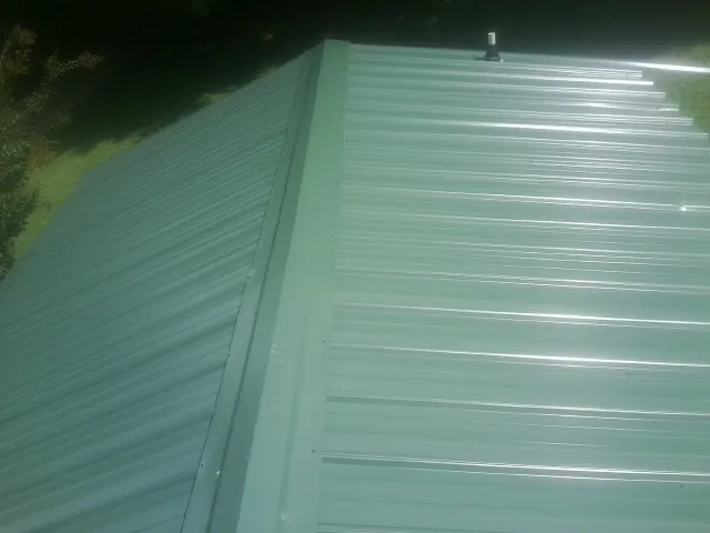 New green metal panels meeting at the ridge of a roof — Flat Roof Repair work by our crew in Foxburg
