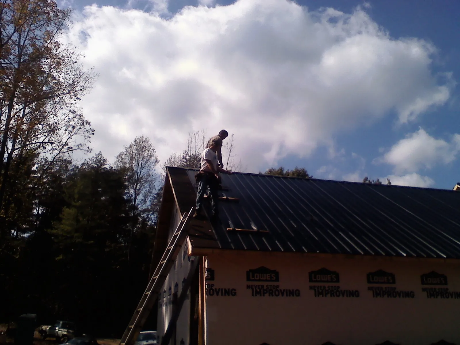 Roofer fastening dark metal panels high against a cloudy sky, from a Roof Inspection job in Foxburg