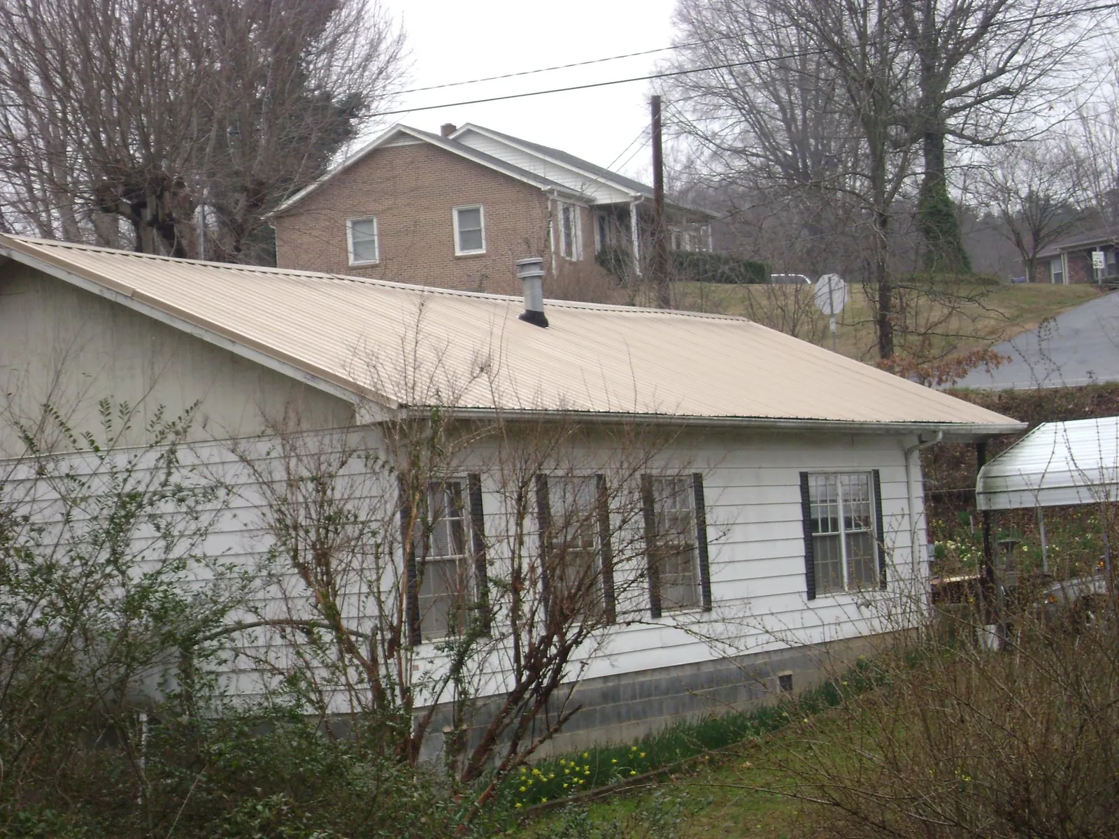 Tan metal roof on a white sided house set into a hillside — Commercial Roofing by Roofing Brothers in Foxburg